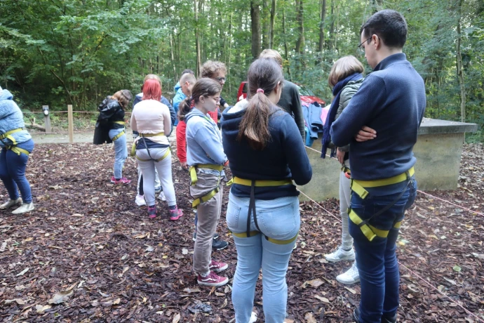 A group of young people standing in a forrest with harnesses around their waists. They are preparing for to go zip lining.
